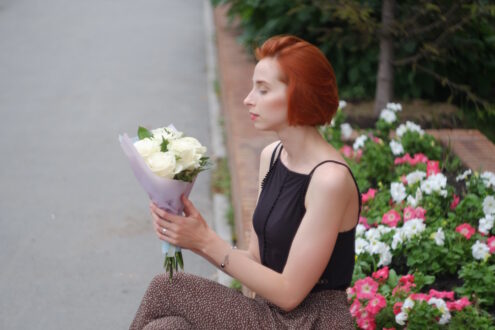 Młoda kobieta o rudych włosach, trzymająca kwiaty