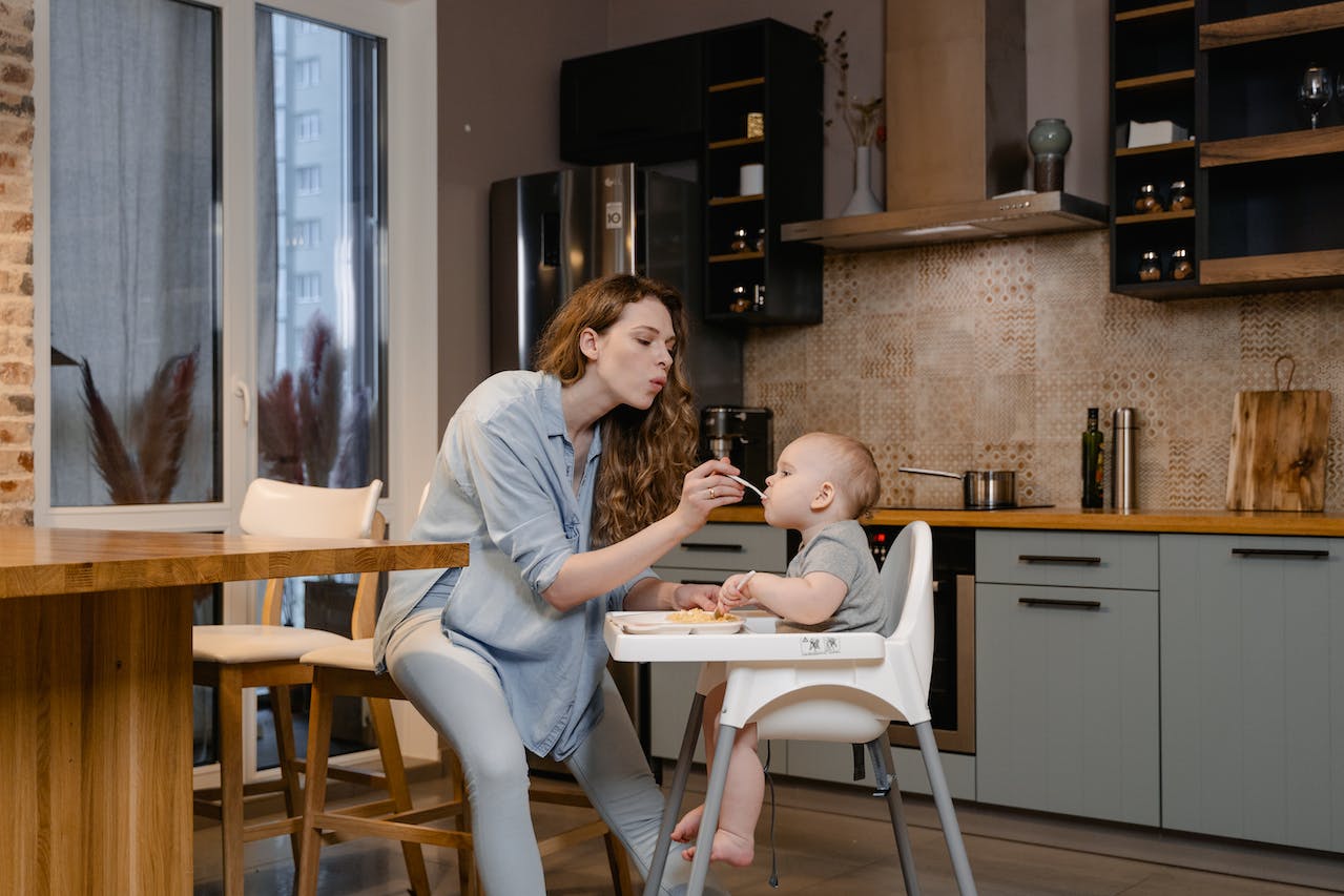 Mama karmi niemowlę siedzące w białym krzesełku do karmienia